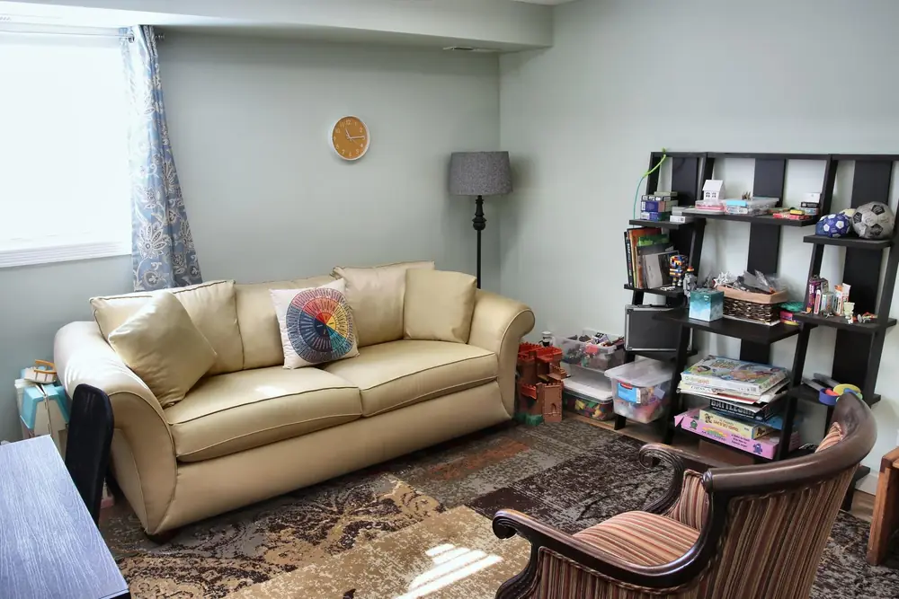 A play therapy room at the Wheaton office, with a tan sofa, a shelf of toys and games, and a patterned rug.