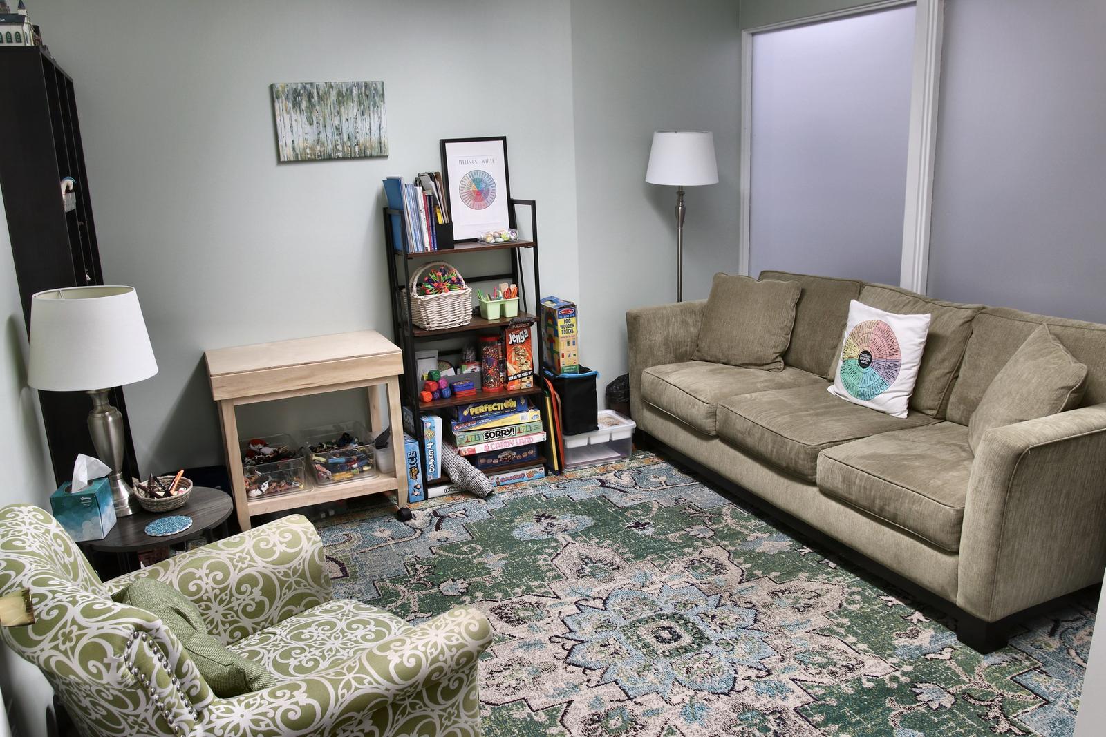 A play therapy room at the Wheaton office, with a sofa, a small play table, shelves of toys, and a green armchair.
