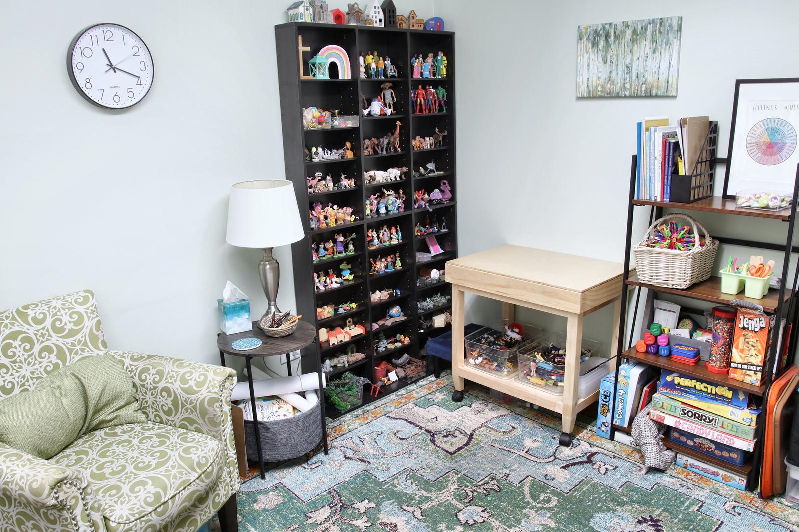 A play therapy room at the Wheaton office, with tall shelves of small figures, a sand tray table, and games.