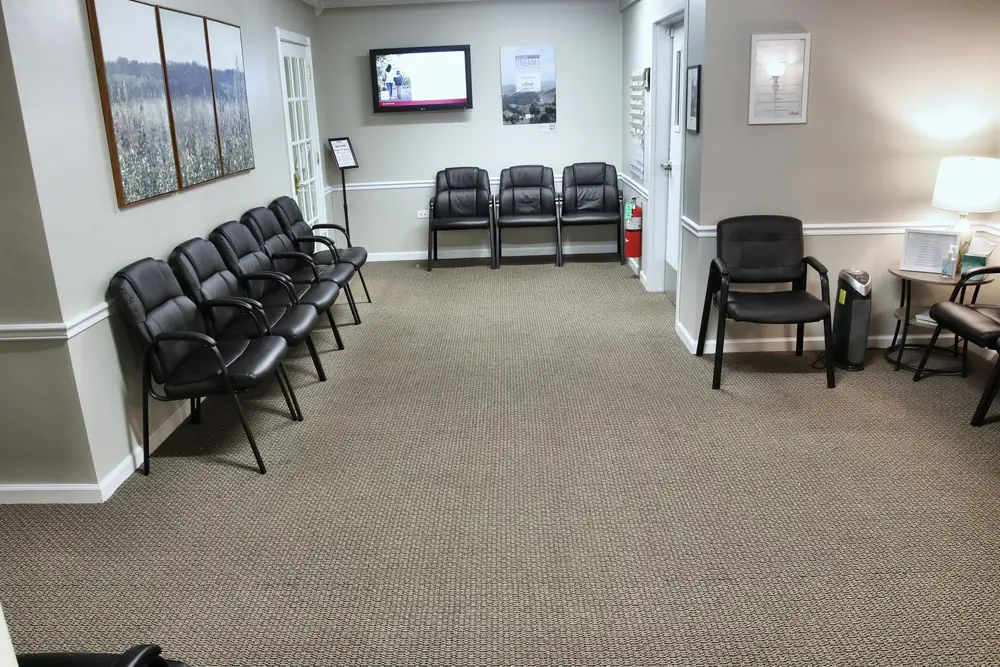 The waiting room at the Wheaton office, with black chairs along the walls, framed meadow prints, and a wall TV.