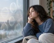 Thoughtful teenager sitting beside a window with circular reflections suggesting recurring thoughts